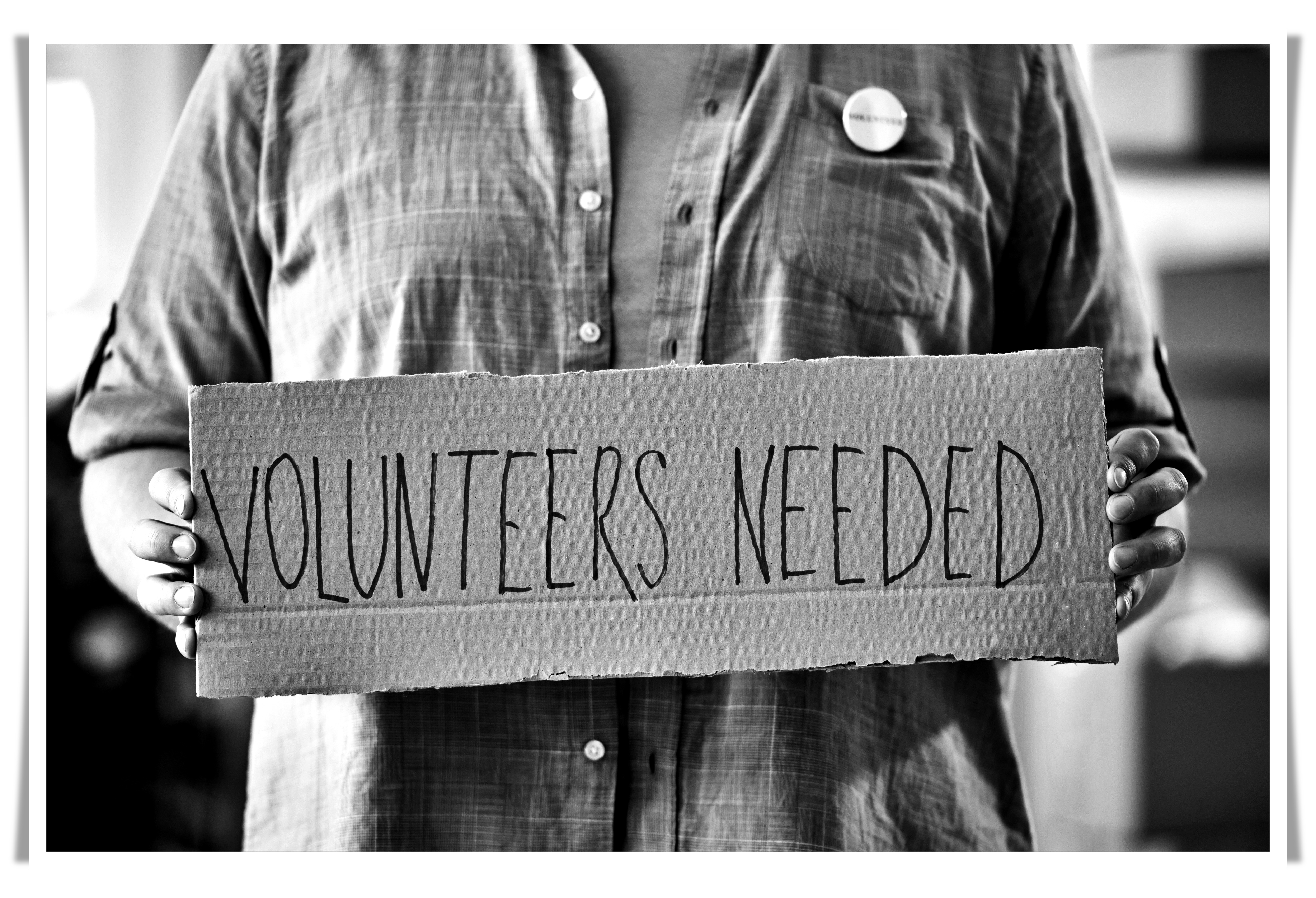 Picture of someone holding a volunteers needed sign.